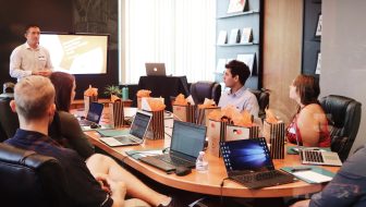 Man standing in front of people sitting beside table with laptop computers